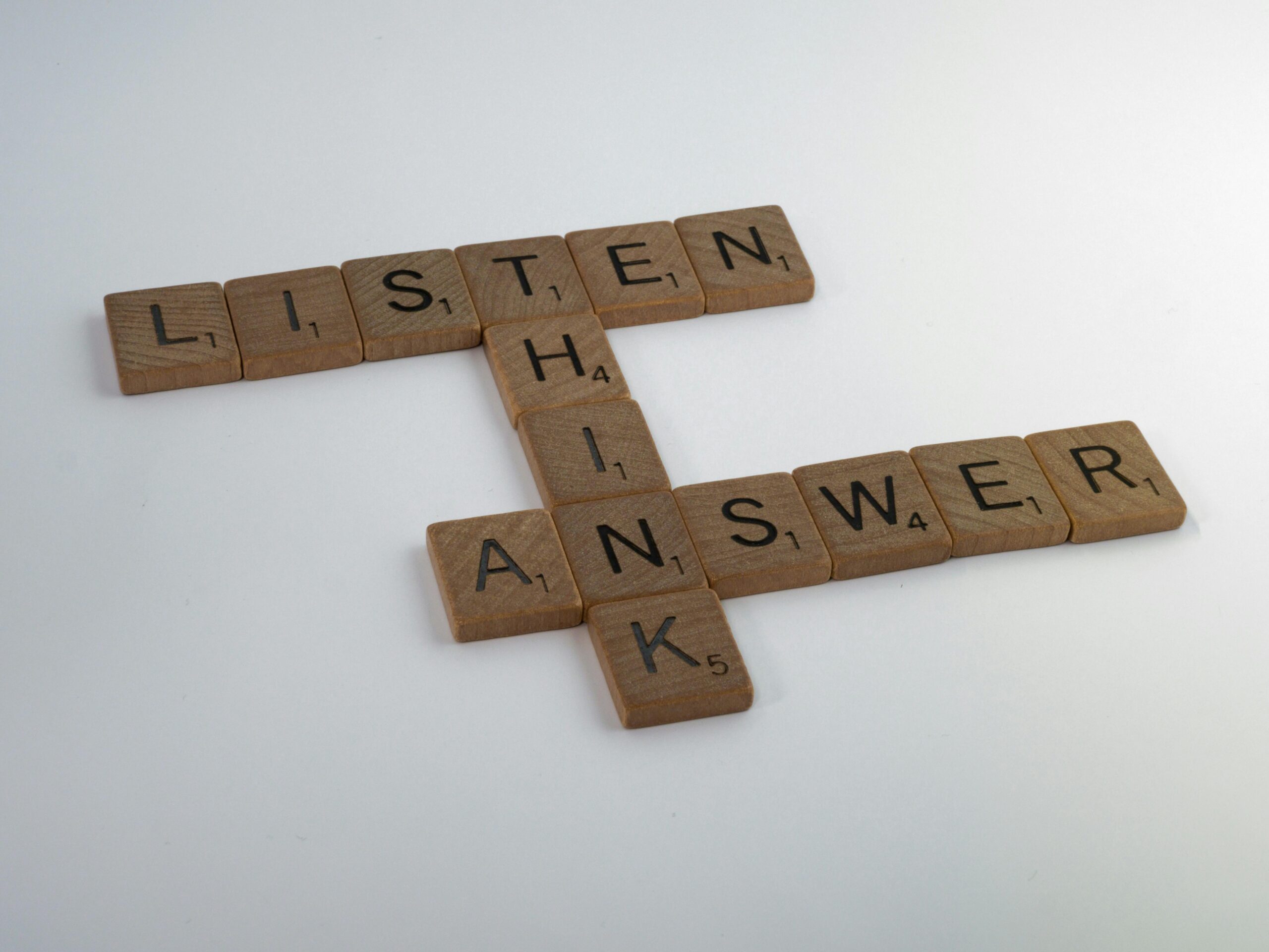 Wooden Scrabble tiles arranged on white surface forming words that inspire thought and communication.